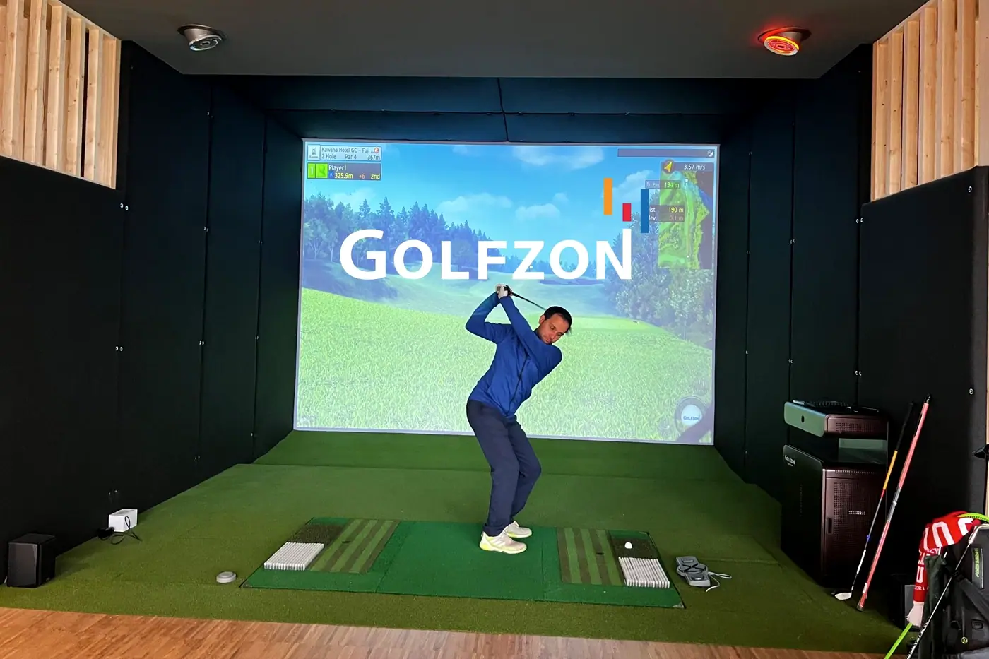 Ein Golfer schwingt in einer Simulator-Box im Studio Götzis vor der GOLFZON-Leinwand